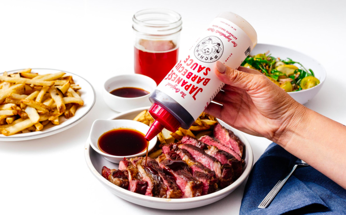bottle of barbecue sauce being poured on sliced steak
