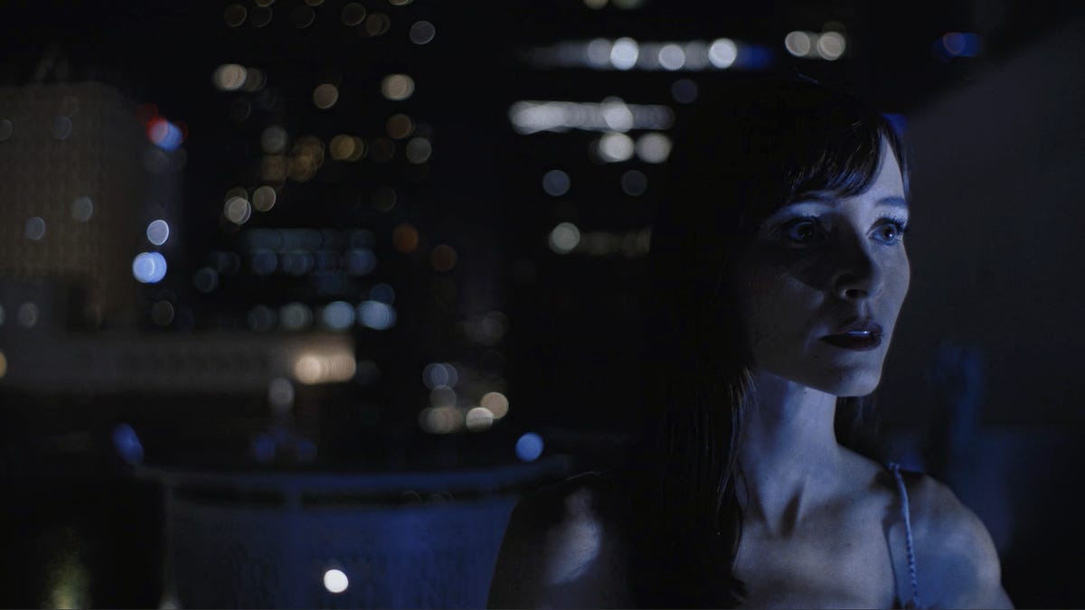 a woman on a rooftop looks offscreen to the rlght