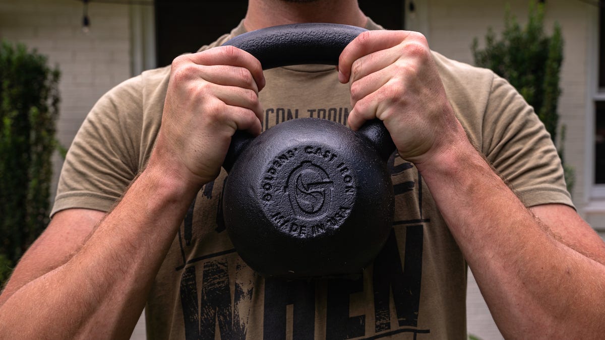 Closeup shot of a buff man's chest, holding a black cast iron kettlebell