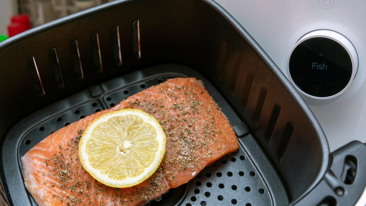 Salmon topped with herbs and lemon in an air fryer basket next to a white air fryer.