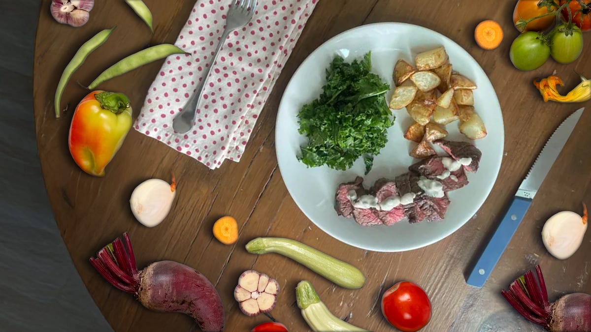 Viewed from above, a plate with food sits on a wood table surrounded by fresh vegetables.