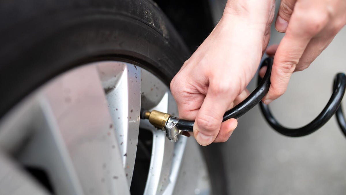 A close-up of a person's hands holding an air hose to fill a car's tire with air.
