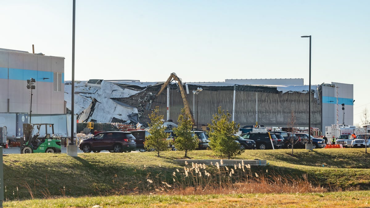 The exterior of the collapsed warehouse from a distance with construction equipment in front of the building.
