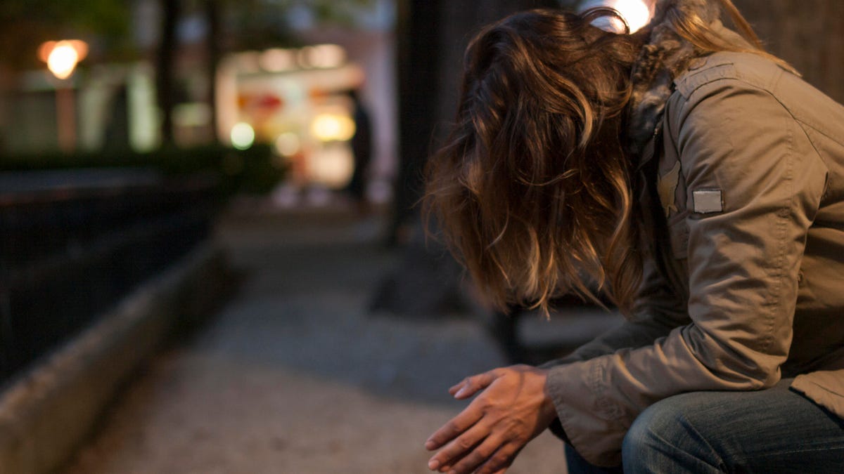 Young woman sitting on a city bench looking down at night