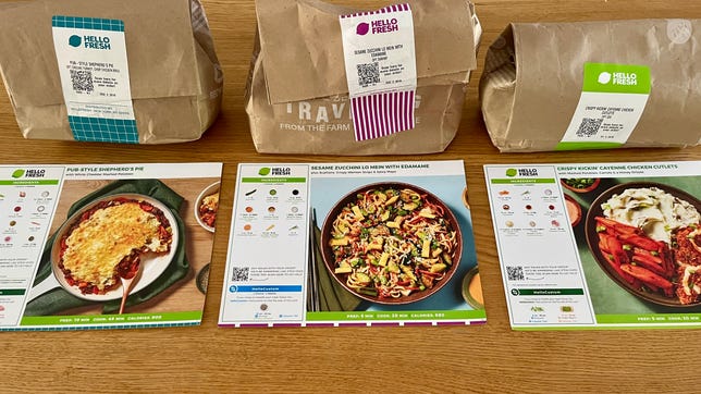 three HelloFresh meal cards and brown paper bags sitting on a counter.