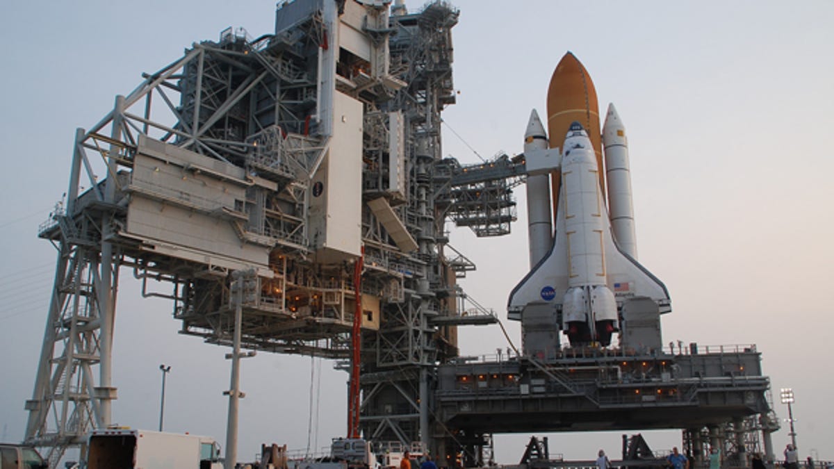 Space shuttle Atlantis stands at launch pad 39A as a cargo canister is lifted into a payload changeout room.