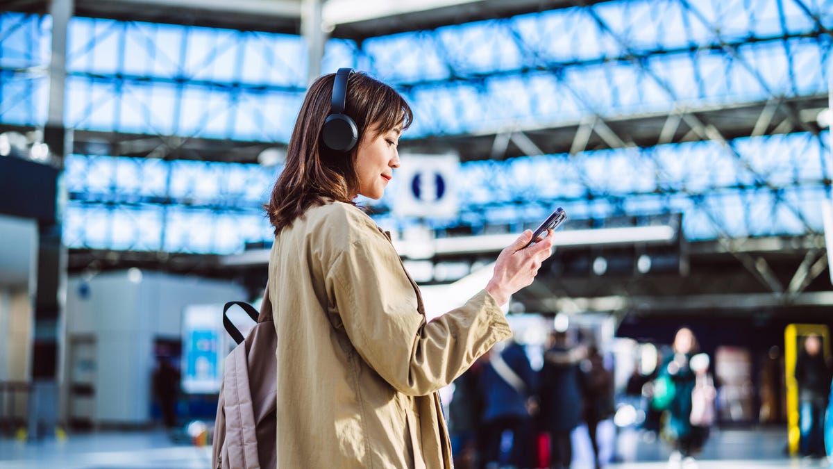 A businesswoman having video call with smart phone and wireless headphones at an airport.