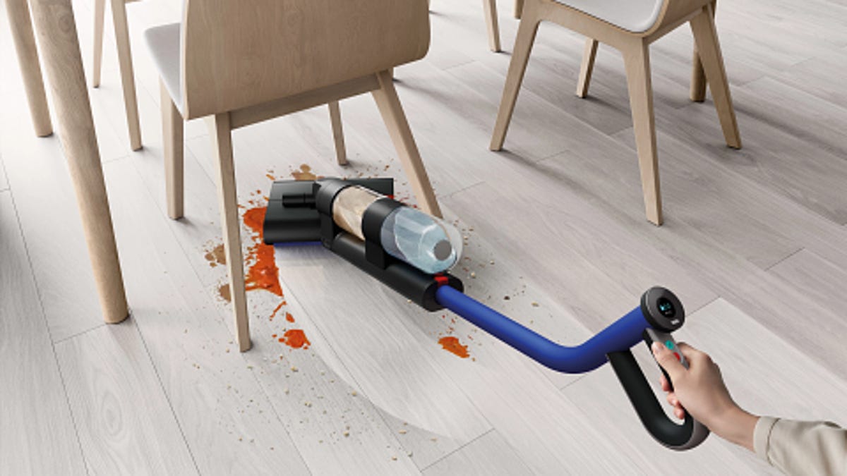 The Dyson WashG1 cleaning a mess on hard flooring under a table.