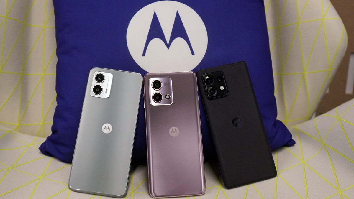 Three phones -- a silver Moto G 5G, light pink Moto G Stylus, and black Moto Edge Plus -- lean on a blue pillow with a Motorola logo.