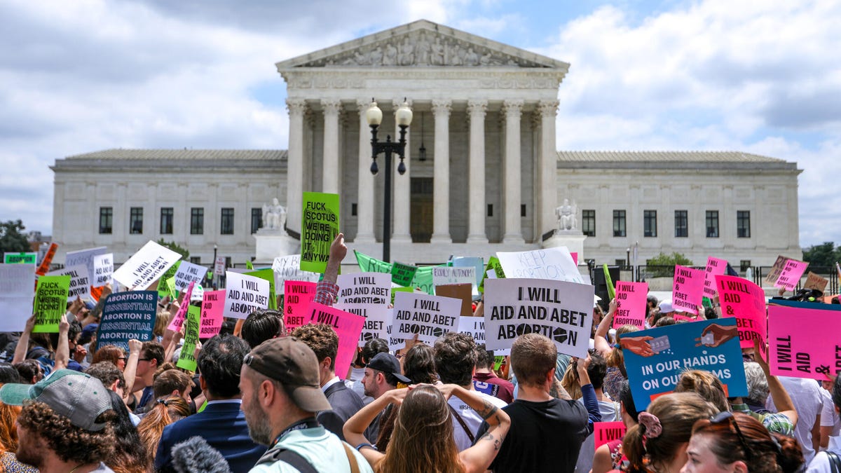 A large crowd holding signs is gathered outside the Supreme Court in Washington, DC