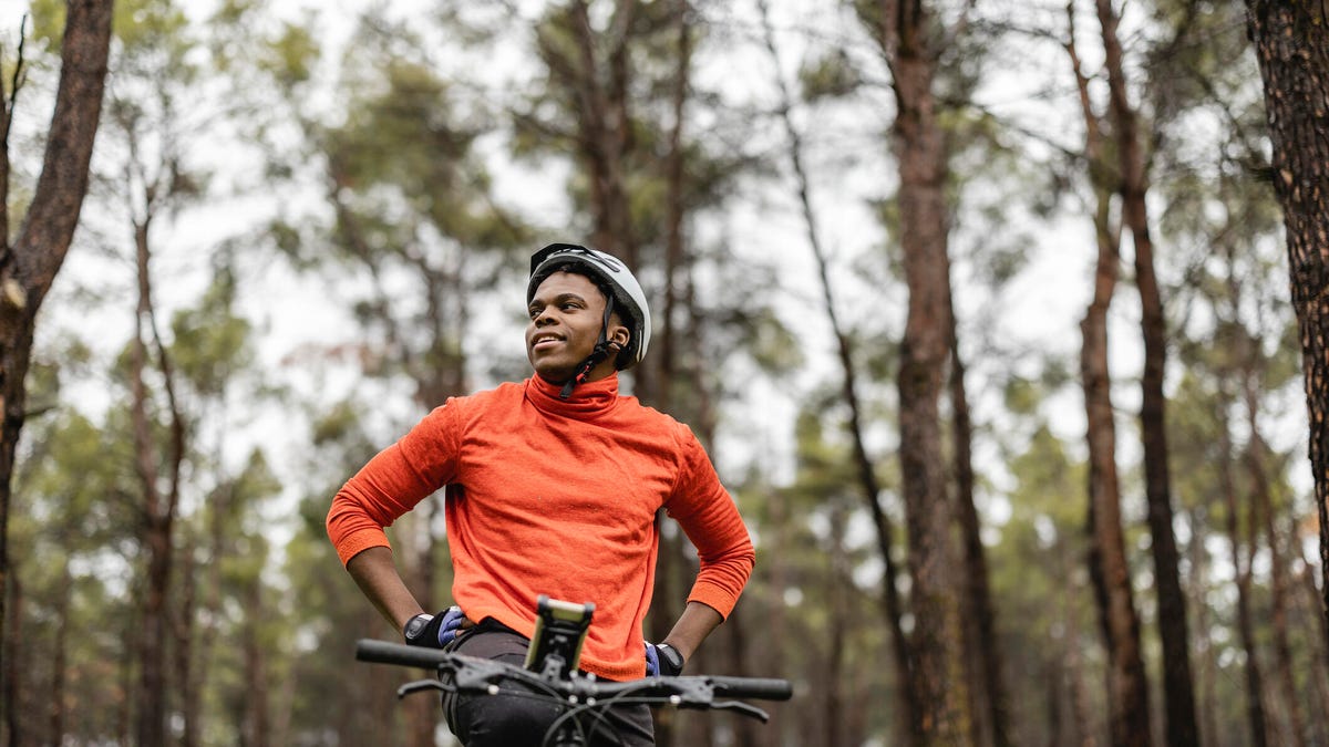 A man sitting on his ebike in a forest, stopping and looking around at the trees. gettyimages-1448688360