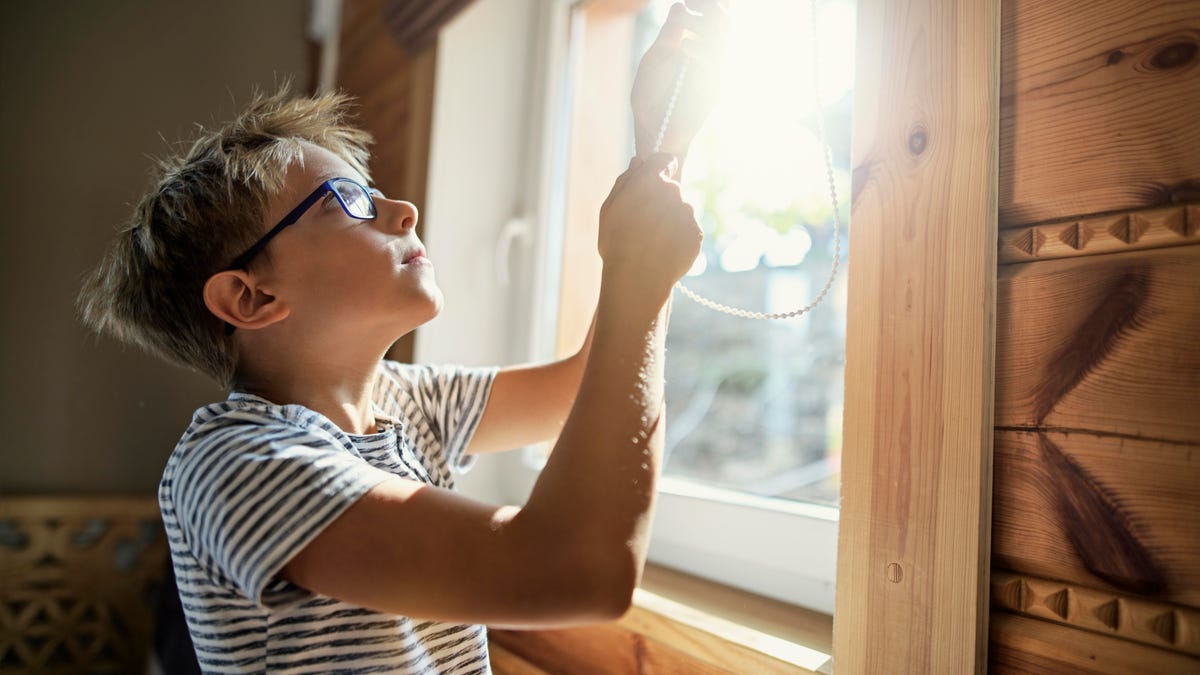 A person lowering blinds for a sunny window