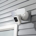 The Lorex floodlight cam mounted on house siding above a glass door.