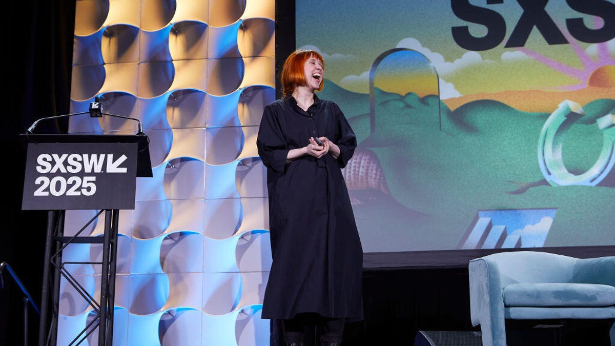 Holly Herndon, a white woman with red hair wearing a black dress, stands on a stage.