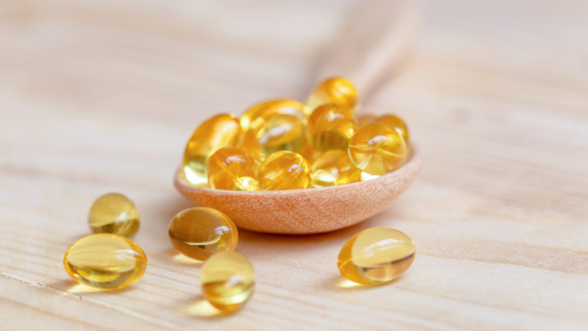 Vitamin E supplements on a wooden spoon, some have spilled onto the table.