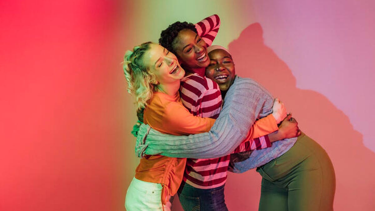 Three people laughing in front of a colorful wall.