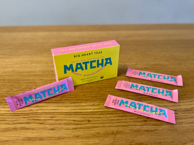 a green and yellow box on a table with small pink packets of matcha around it