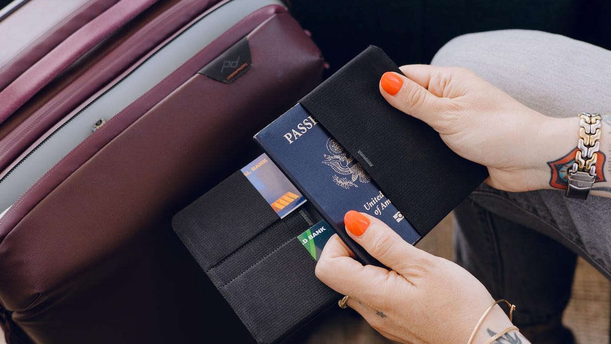 A person holding a document sleeve with a passport slipping into a pocket and credit cards slid into other pockets.