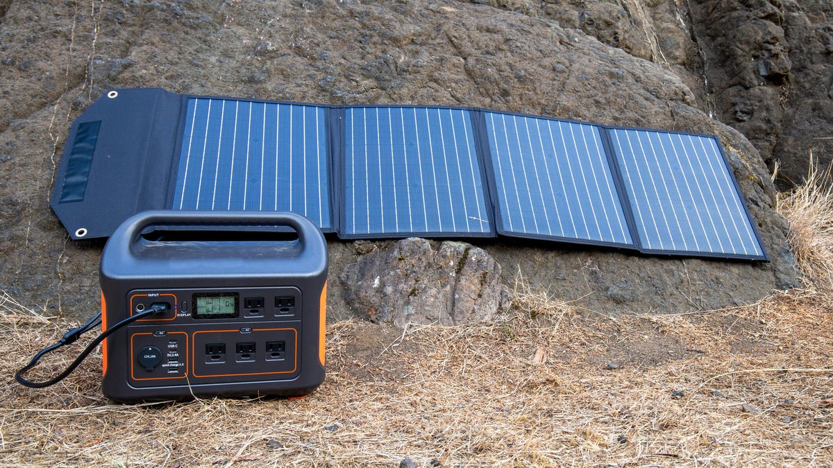 A portable power station and portable solar panels sitting on the ground outside.