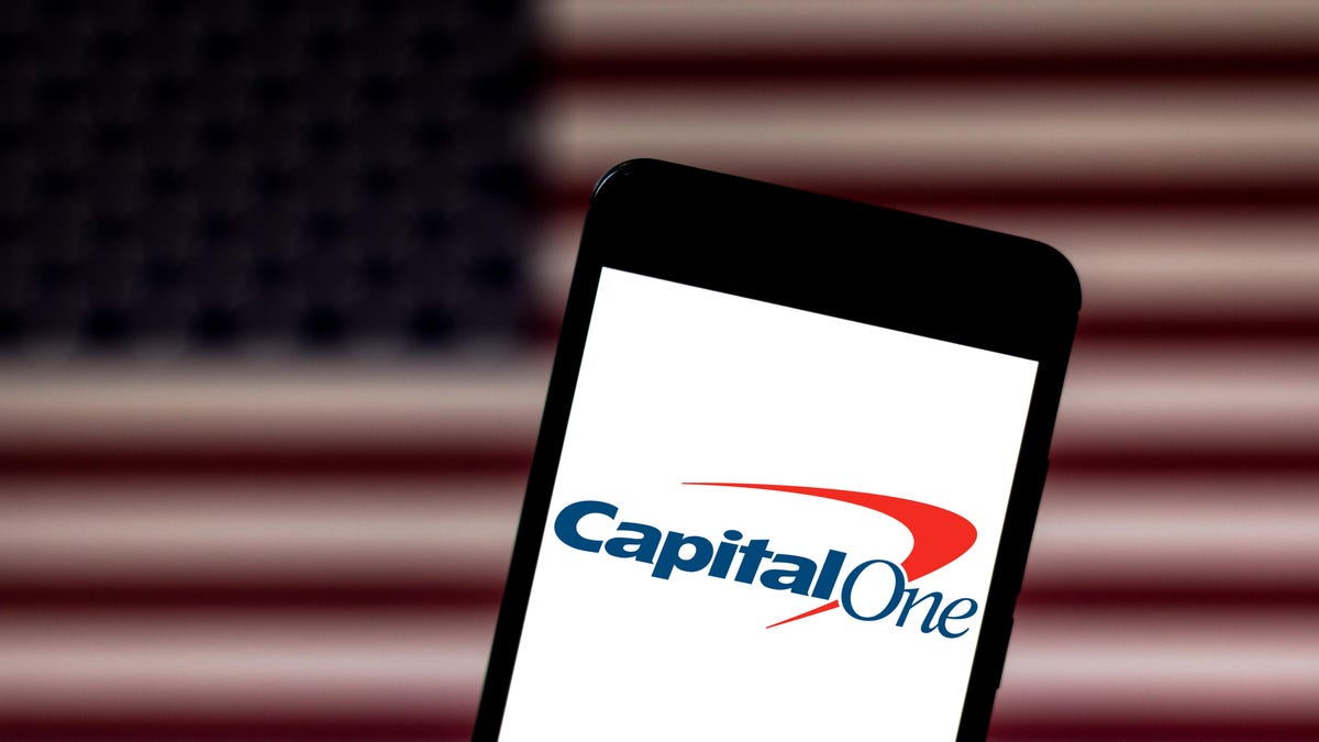 The Capital One logo is visible on a phone screen with the American flag in the background.