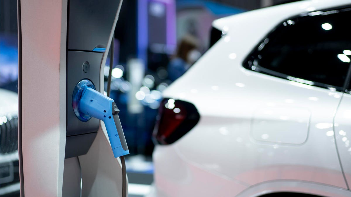 An electric vehicle charger with a white electric vehicle sitting in the background.