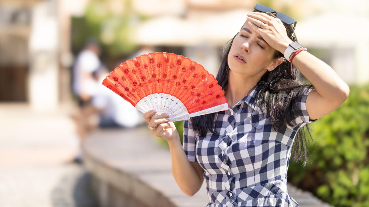 A woman fanning herself with a red fan, feeling hot