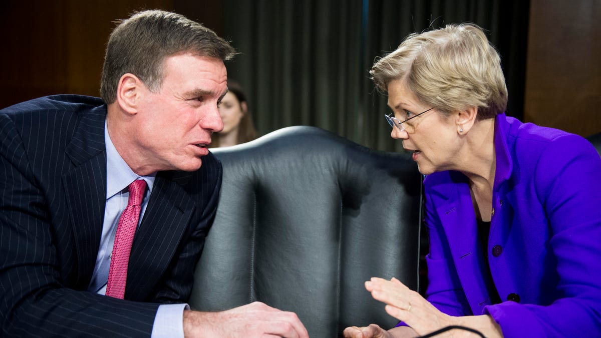 Sen. Mark Warner and Sen. Elizabeth Warren talk with each other in a Senate meeting room before the start of a hearing in 2015.