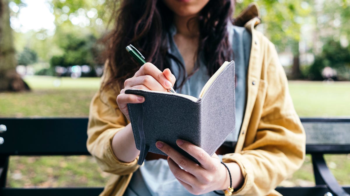 Close up of woman journaling on a bench in a park.