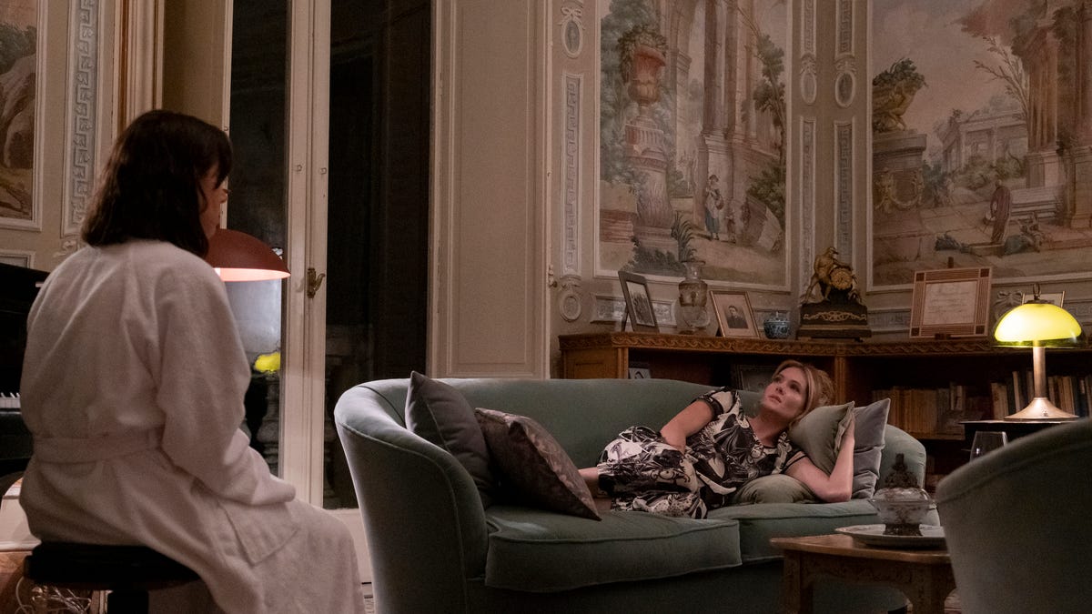 Aubrey Plaza and Meghann Fahy in a large, ornate room with people and old scenes painted on the walls