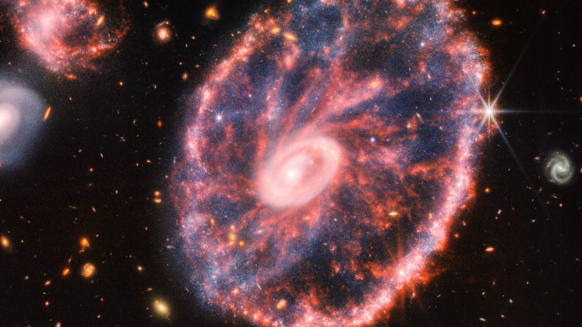 A round, reddish galaxy with a circular center glows against a dark starry background.
