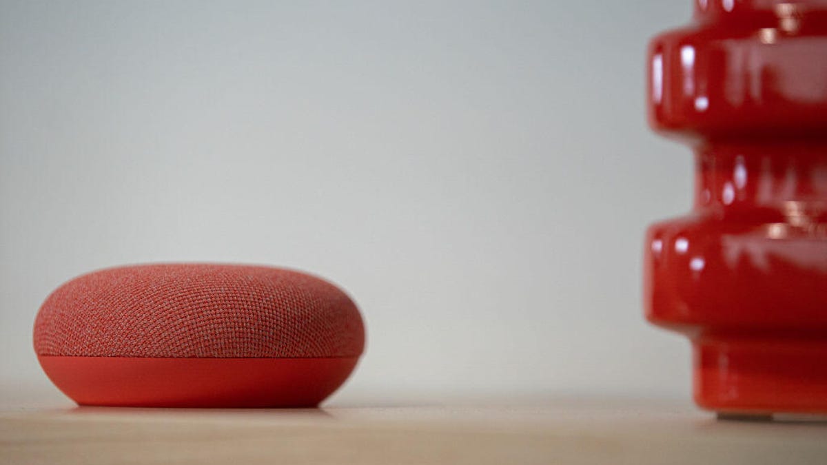 A red Nest Mini speaker on a wood table next to a red decoration.
