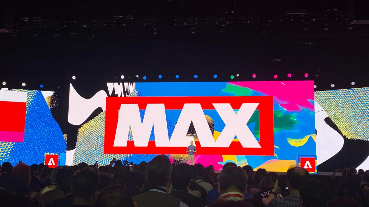 presenter on stage in front of a screen that reads MAX
