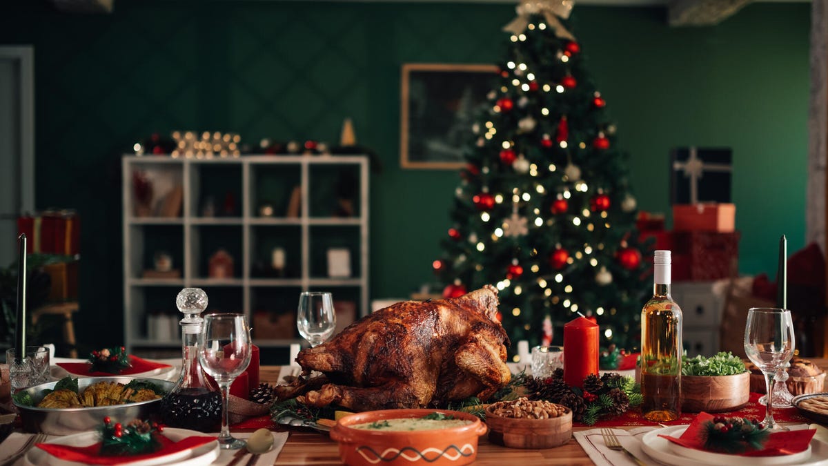 A photo of a dining table with a turkey and wine and plates, with a Christmas tree in the background.