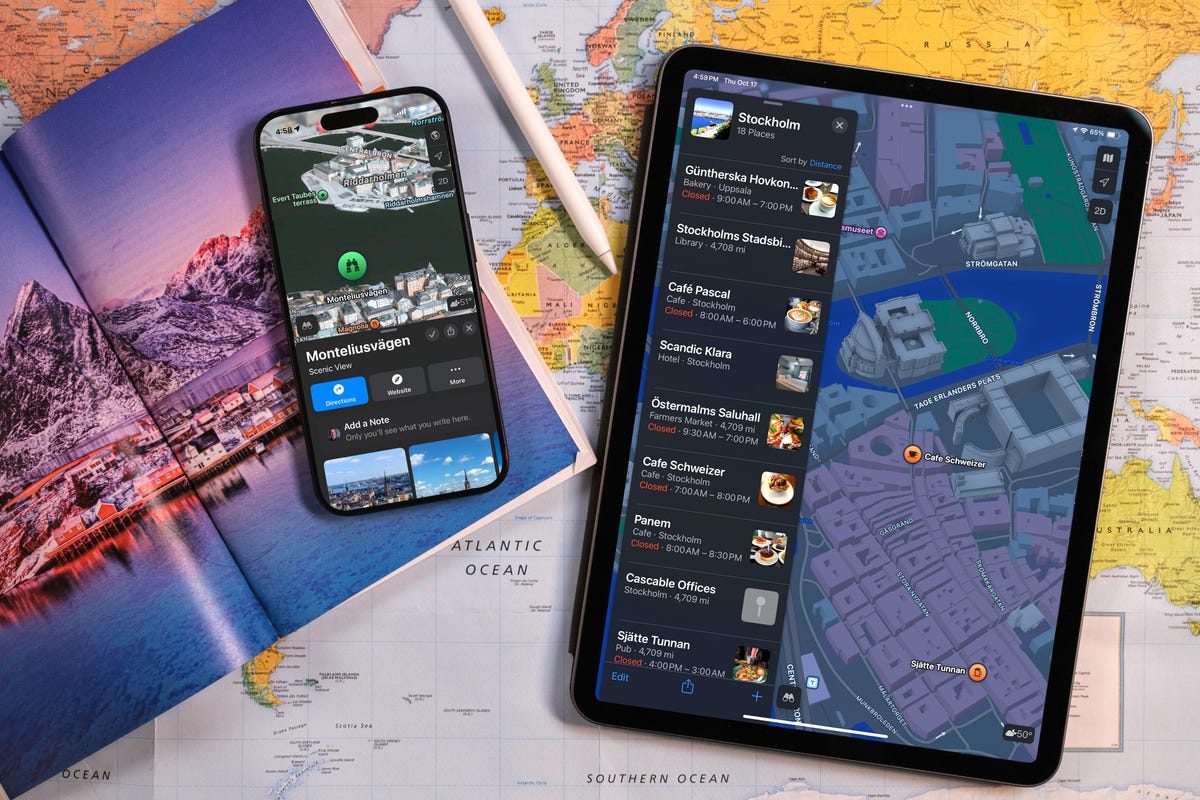 A table covered in a paper map of the world, with a guidebook, an iPhone, an iPad, and an Apple Pencil scattered on top of the map. Both screens are showing the Apple Maps app.