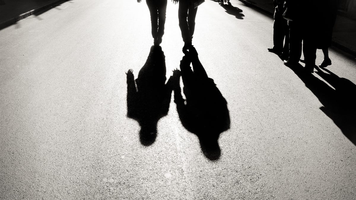 Two shadows on a street as people walk in the distance. "Shadow profiles" include information about you that you didn't directly share with Facebook.
