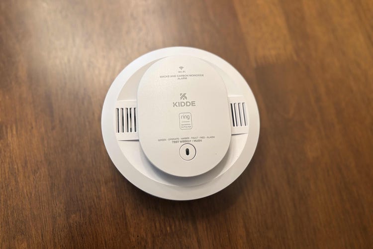A Ring-enabled Kidde smoke detector on a wooden table. 