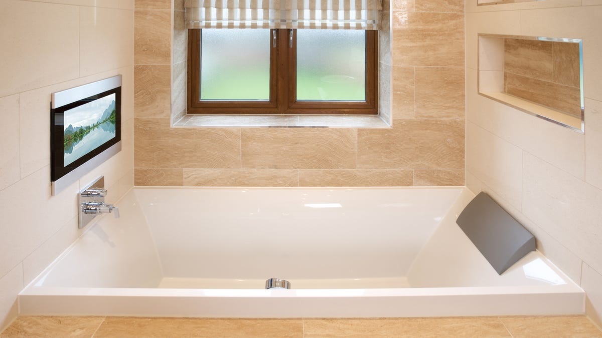 A bathroom with a TV mounted above the bathtub faucet