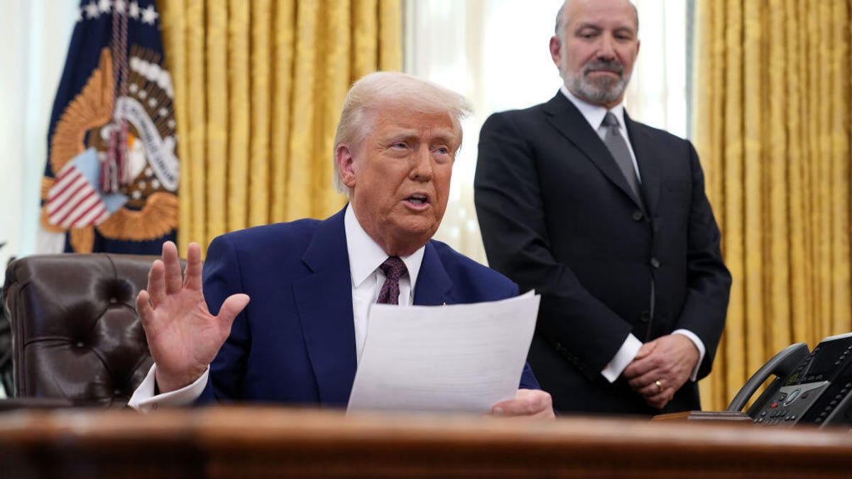 trump-at-desk-with-howard-lutnick-standing-behind-him