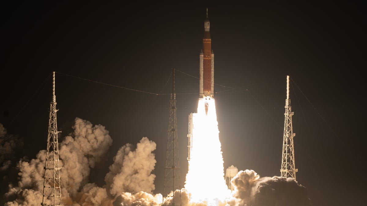 Against the night sky, NASA's Artemis I rocket is seen engulfed in smoke and flames, on its way to space.