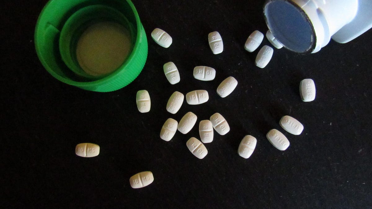 Zyrtec tablets on a black surface next to open bottle and green cap.