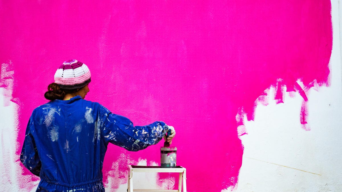A photo of a woman painting a wall bright pink (gettyimages-1307283295)