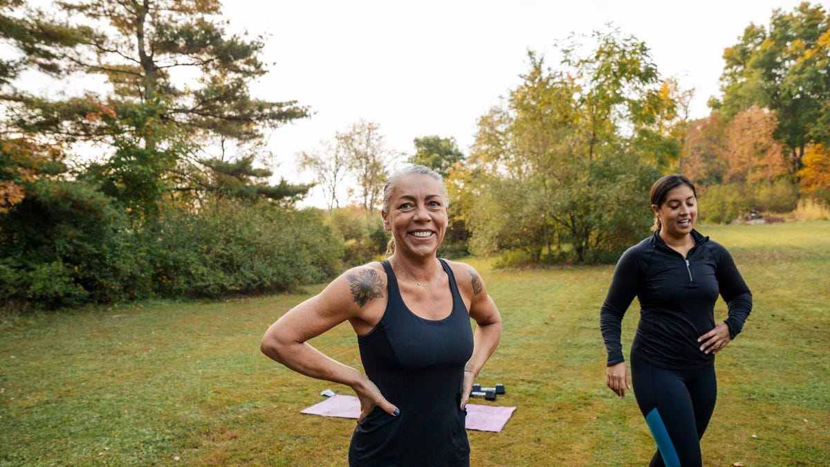 Two smiling people in workout clothes in a park.