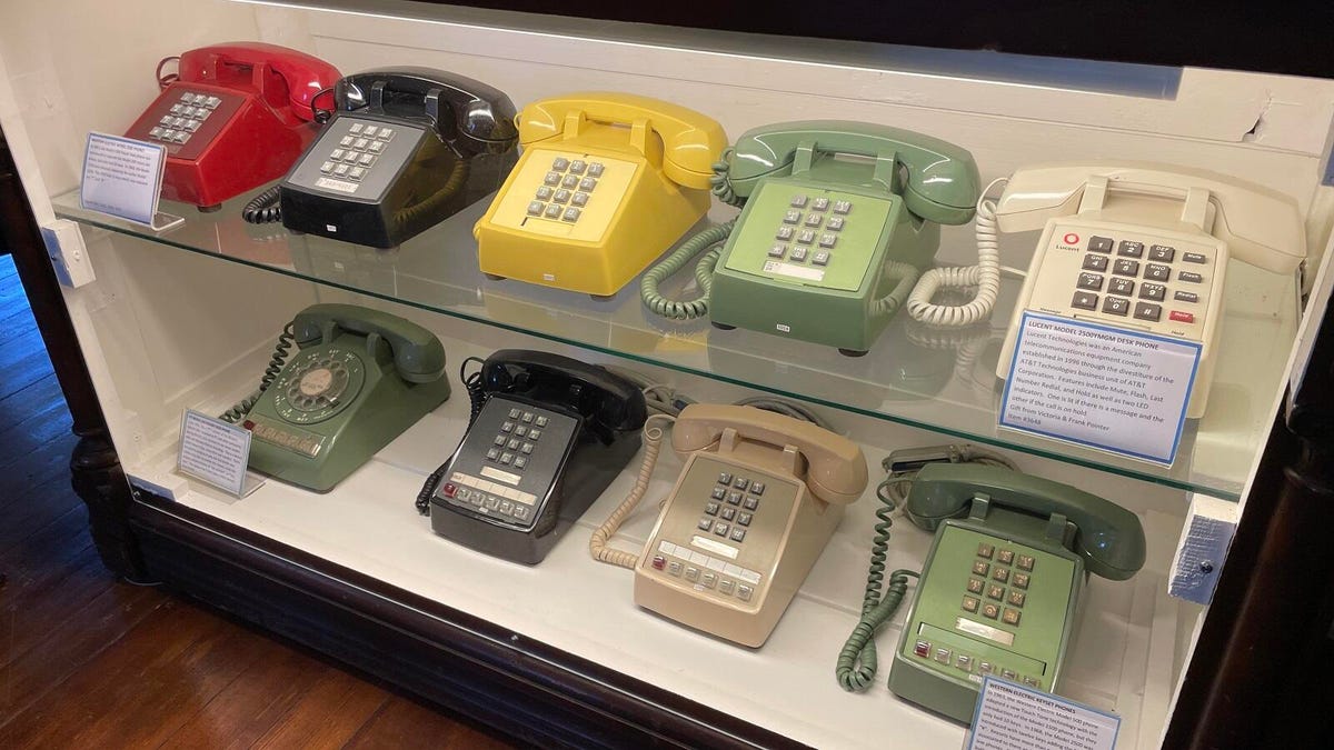 Nine phones in a case, all different colors, all iconic Western Electric models with the heavy trapezoidal base with numbers or dials and cradling the handset.