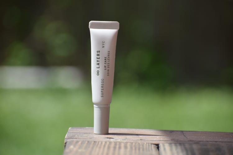 The Superegg peptide lip balm on a wood surface in front of a grassy blurred background.