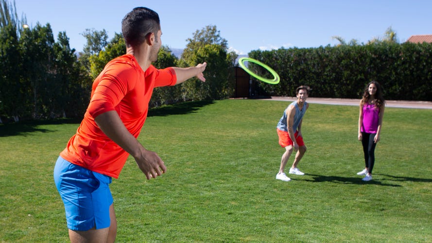 A person in an orange top throwing a green ring to two other people