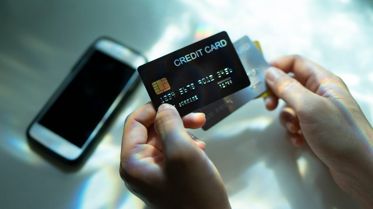 Top view Hand holding credit card black and another hand using phone with spectrum light and shadow background