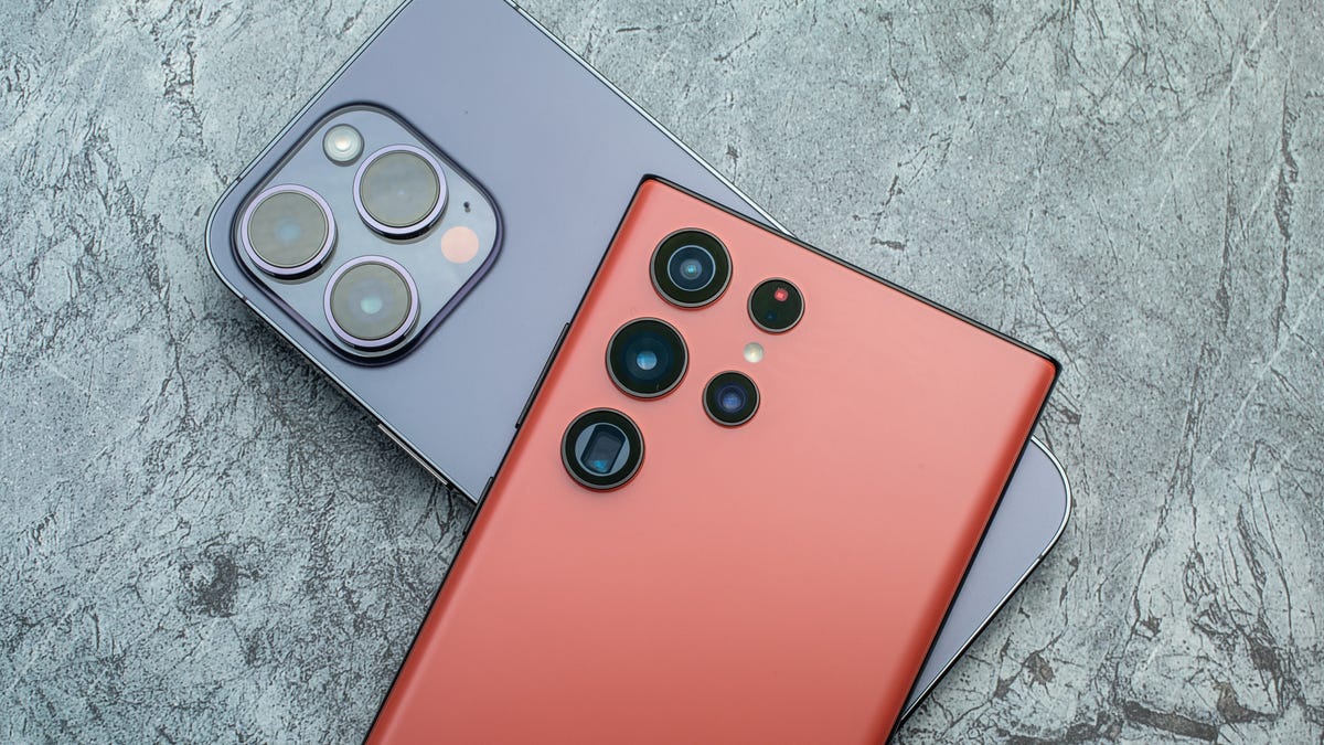 The back of Samsung's Galaxy S22 phone rests atop the back of an Apple iPhone 14 Pro.