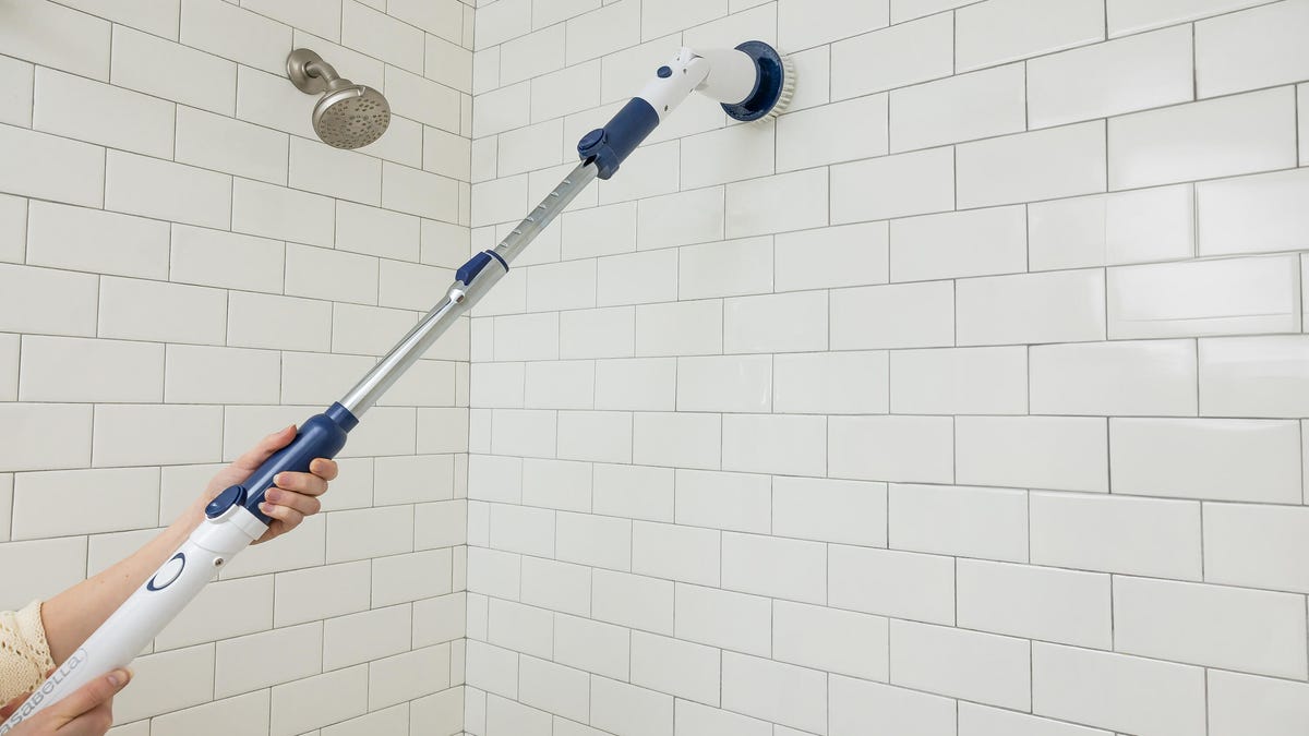 a person holding Casabella's Power Spin Scrubber on their shower tiles