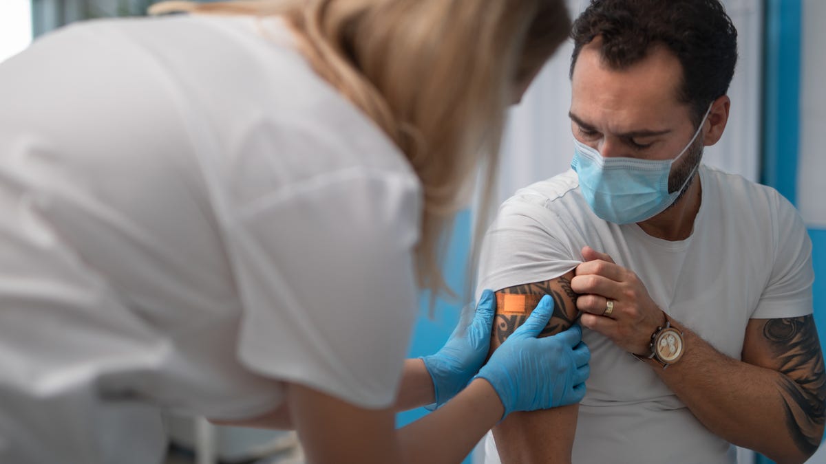 A person with a tattoo getting a Band-Aid applied to their vaccination site