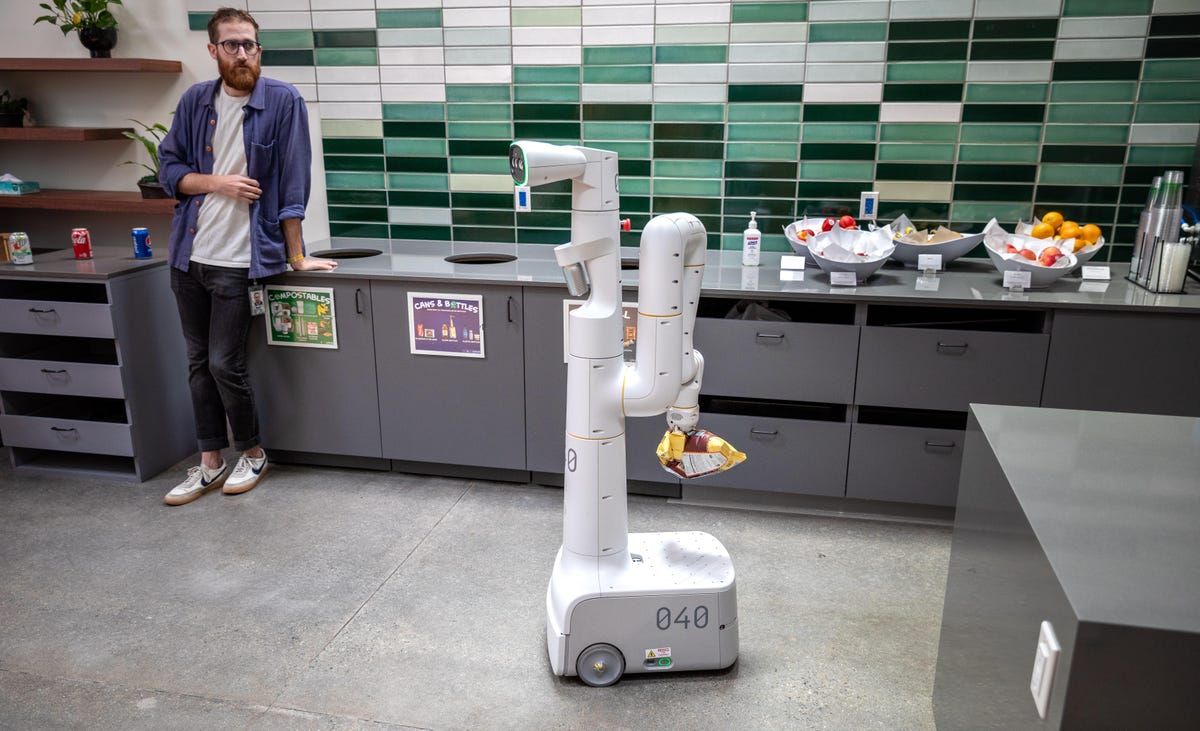 A wheeled robot carries a bag of chips through a Google office kitchen